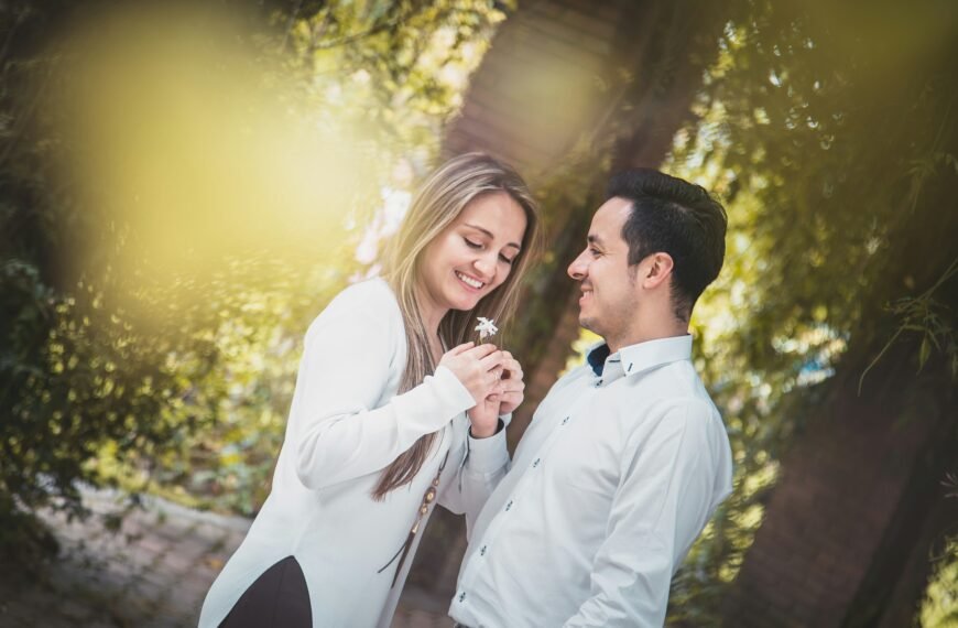 man giving white flower to woman surrounded by green trees